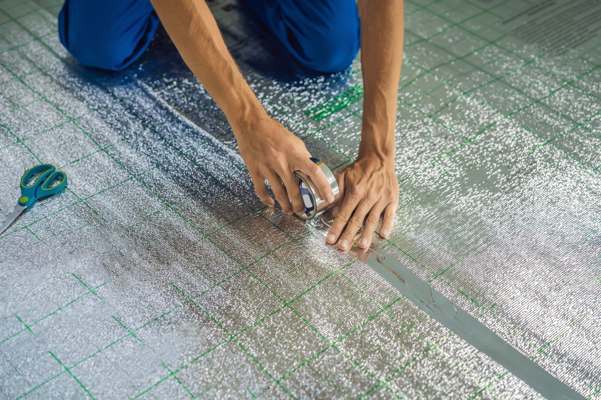 Master installs the overlapping thermal insulation in the room. Floor heating installation. Male hand holds reinforced tape. Repair in the apartment, floor insulation Master installs the overlapping thermal insulation in the room. Floor heating installation. Male hand holds reinforced tape. Repair in the apartment, floor insulation